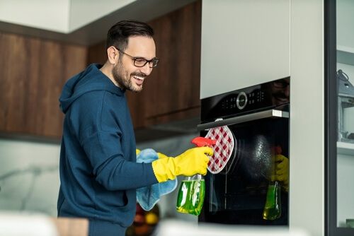 בחור מנקה את התנור שלו לפי המדריך ניקיון תנורים